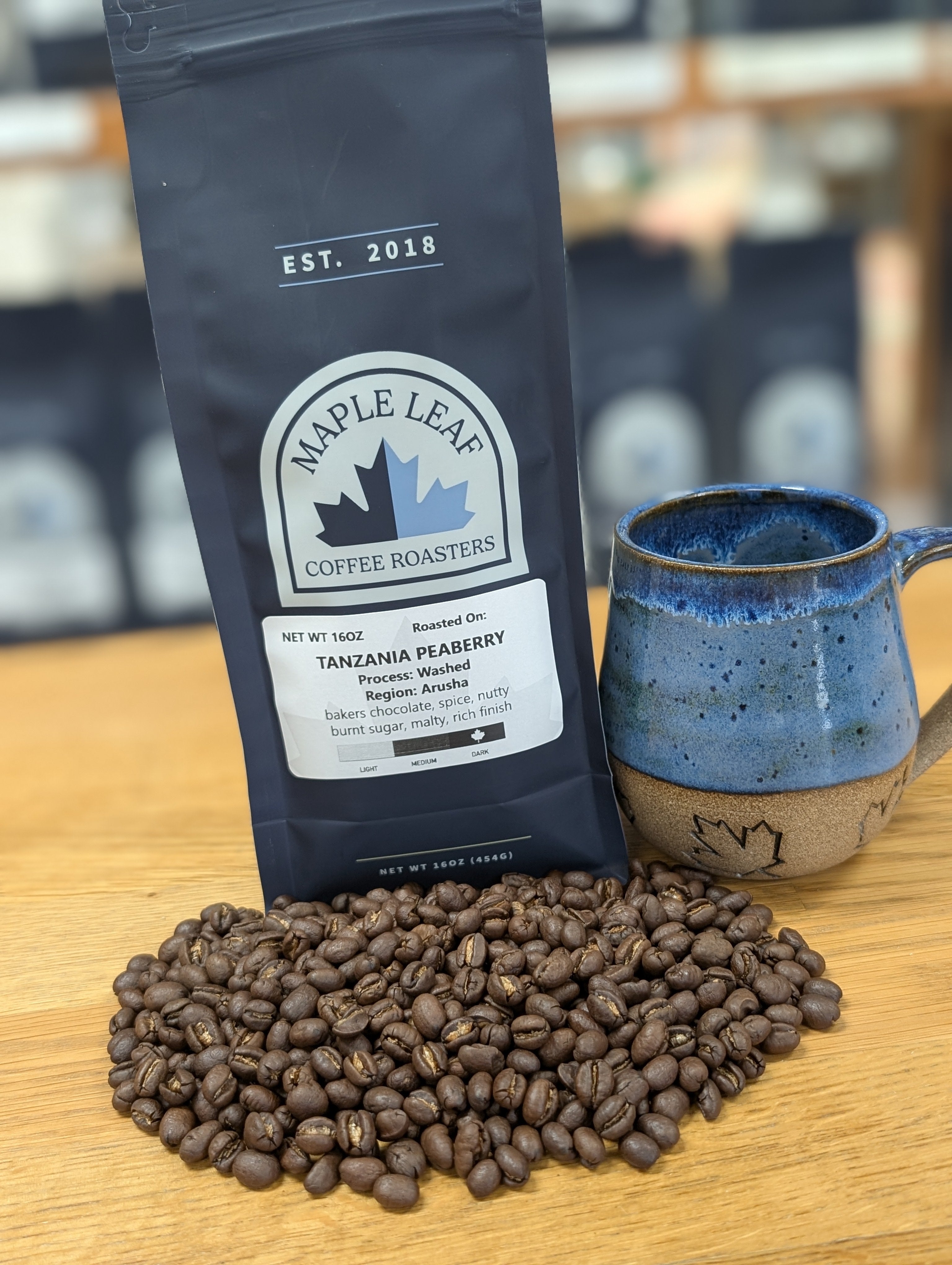 Maple Leaf Coffee Roasters package with coffee beans and a blue mug on a wooden surface.