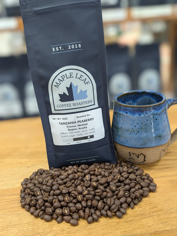 Maple Leaf Coffee Roasters package with coffee beans and a blue mug on a wooden surface.
